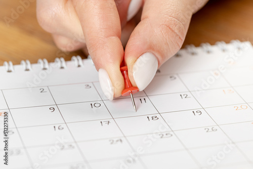 beautiful female Hand with manicure pushes a red pin on a calendar 11 day