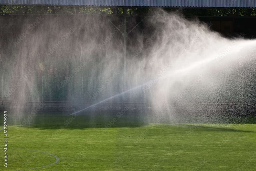 Podlewanie trawy w słonecznej suszy na boisku sportowym. - obrazy, fototapety, plakaty 