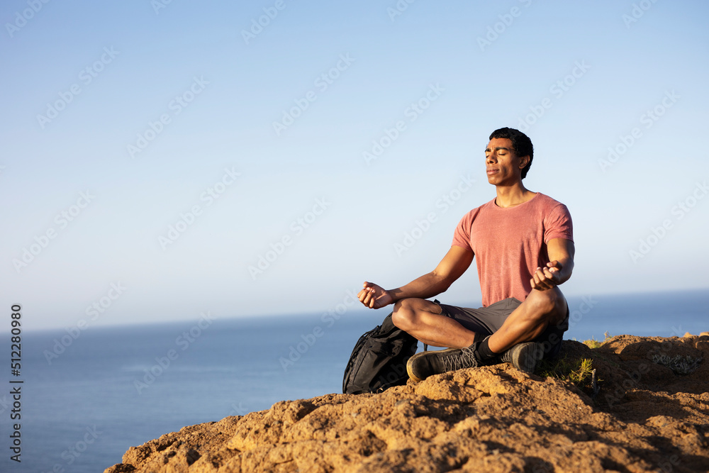 Young man meditating on top ocean cliff.