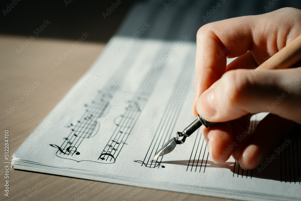 Sheet with notes and a woman's hand drawing notes with an ink pen, writing music, selective focus Sheet with notes and a woman's hand drawing notes with an ink pen, writing music, selective focus