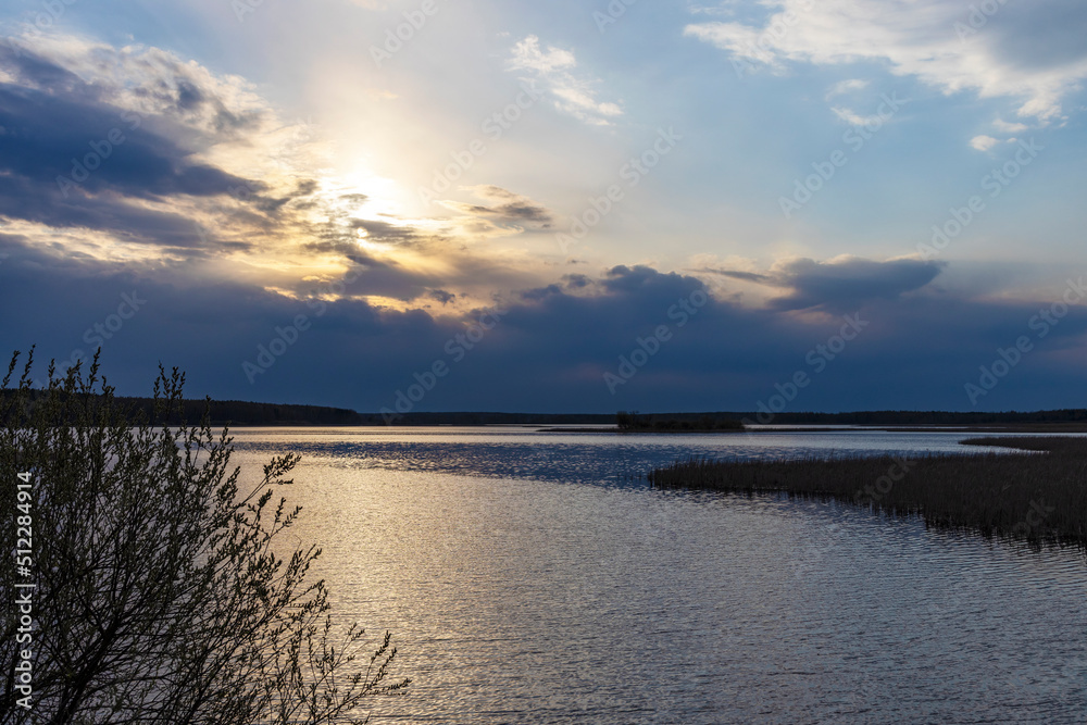 Evening dramatic landscape, lake in spring, sun shining through blue clouds. Ripples on the water from a strong wind.