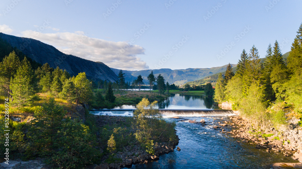 Summer landscape with blue sky, river, lake, forest and mountains. Wild Scandinavia in warm sunset light
