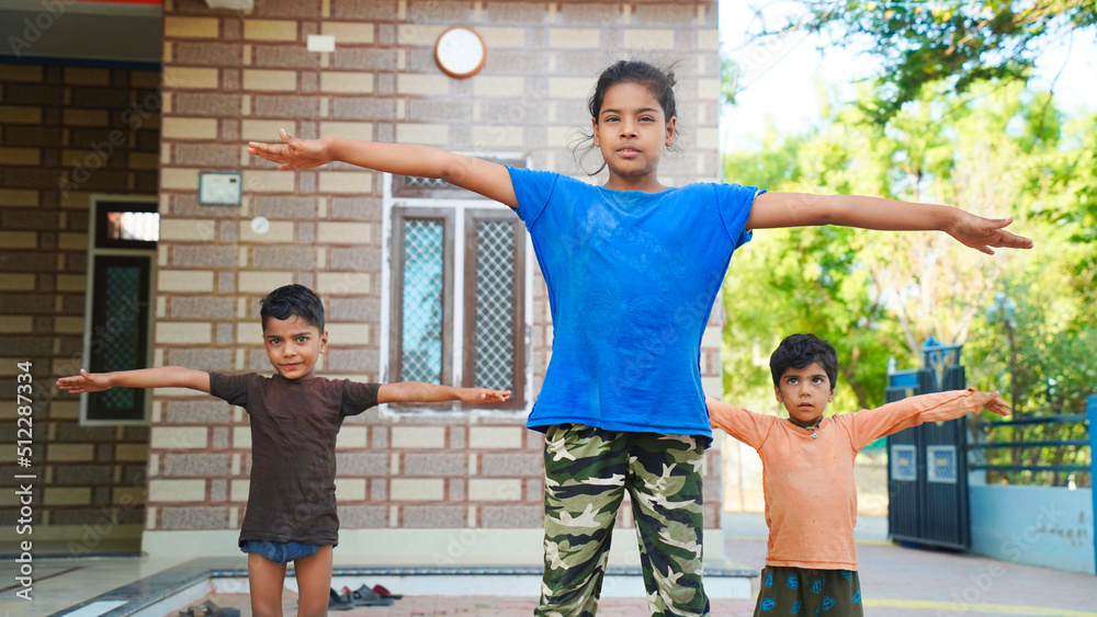 Three Indian little kids doing meditate yoga asana on roll mat at home.