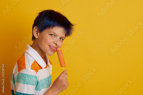 young guy eating appetizing ice cream on a stick on a yellow background