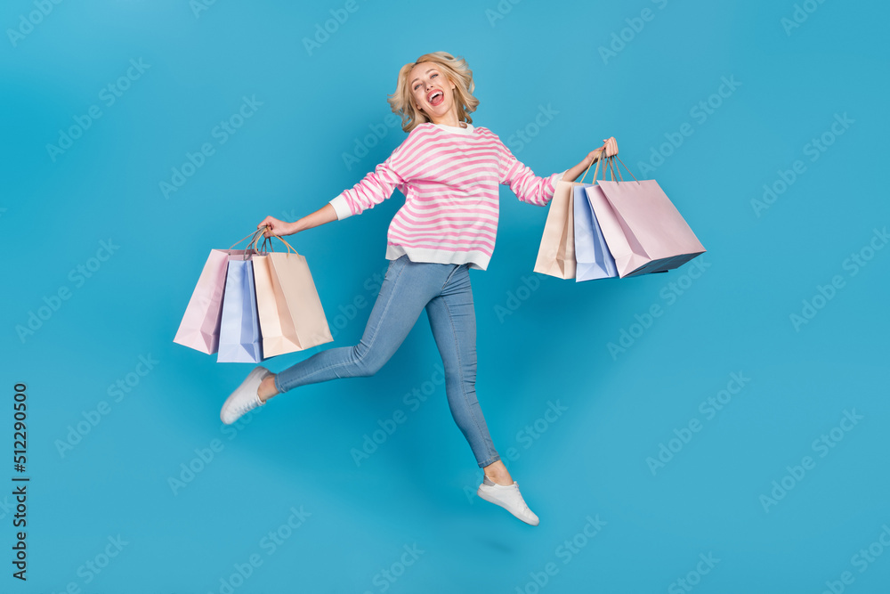Photo of excited pretty woman wear striped sweater jumping running rising bargains isolated blue color background Photo of excited pretty woman wear striped sweater jumping running rising bargains isolated blue color background