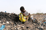 Little African girl sitting on a rubbish heap looking for recyclable materials to help her parents in need