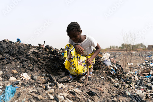 Little African girl sitting on a rubbish heap looking for recyclable materials to help her parents in need