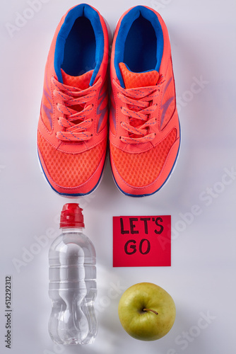 Vertical shot flat lay pair of shoes with water bottle and green apple. Sticker note with lets go inscription. photo