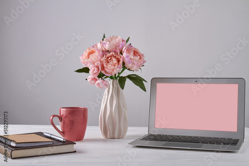 Vase of flowers with notepads and laptop with copy space. Notebook with pen and red cup. photo