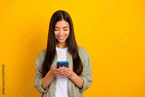 Photo of young pretty good mood girl blogger chatting with boyfriend in smartphone isolated on yellow color background