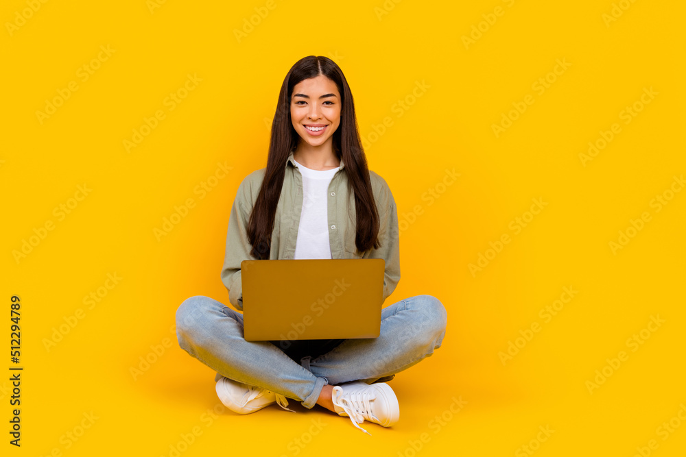 Full size portrait of cheerful pretty lady sit floor hold netbook typing email isolated on yellow color background Full size portrait of cheerful pretty lady sit floor hold netbook typing email isolated on yellow color background