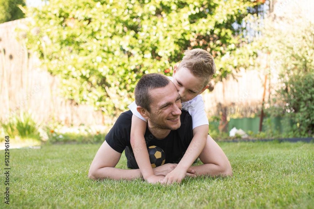 A cute baby is lying on his father's back. Lying on the lawn