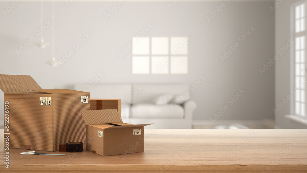 Wooden table, desk or shelf with stack of cardboard boxes over blurred view of white living room with sofa, modern interior design, moving house concept with copy space Wooden table, desk or shelf with stack of cardboard boxes over blurred view of white living room with sofa, modern interior design, moving house concept with copy space