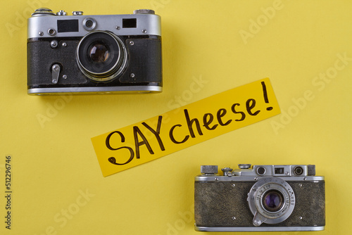 Two vintage photo cameras on yellow background. Say cheese handwriting. photo