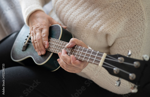Hands of an elderly woman 70+ sitting on the sofa at home and playing the ukulele. Adaptation of pensioners in the modern world. New knowledge and skills. Prevention of Alzheimer's disease, sclerosis 