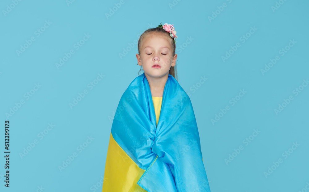 Portrait of upset patriot child girl with Ukrainian flag on blue studio background. Pray for Ukraine Portrait of upset patriot child girl with Ukrainian flag on blue studio background. Pray for Ukraine
