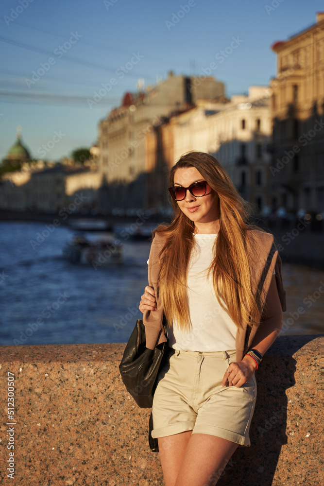 beautiful happy woman in sunglasses with long hair in a european city, in the sunbeams, walks along the bridge in st. petersburg. city walks in summer, tourism
