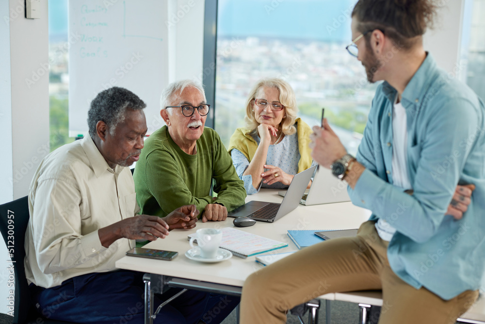 A young teacher asks a small group of multiracial senior students questions about digital marketing in a classroom. A young teacher asks a small group of multiracial senior students questions about digital marketing in a classroom.