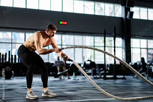 powerful man training battle ropes at cardio workout in dark gym. Professional athlete exercise fitness sport club equipment. Strong bodybuilder lifting weights. Athletic person effort © Guys Who Shoot