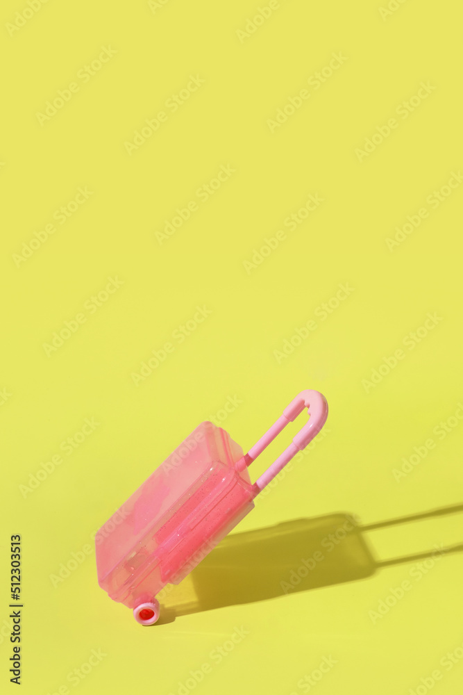 Toy pink suitcase on yellow background with a hard shadow. Copy space. Travel or migration concept