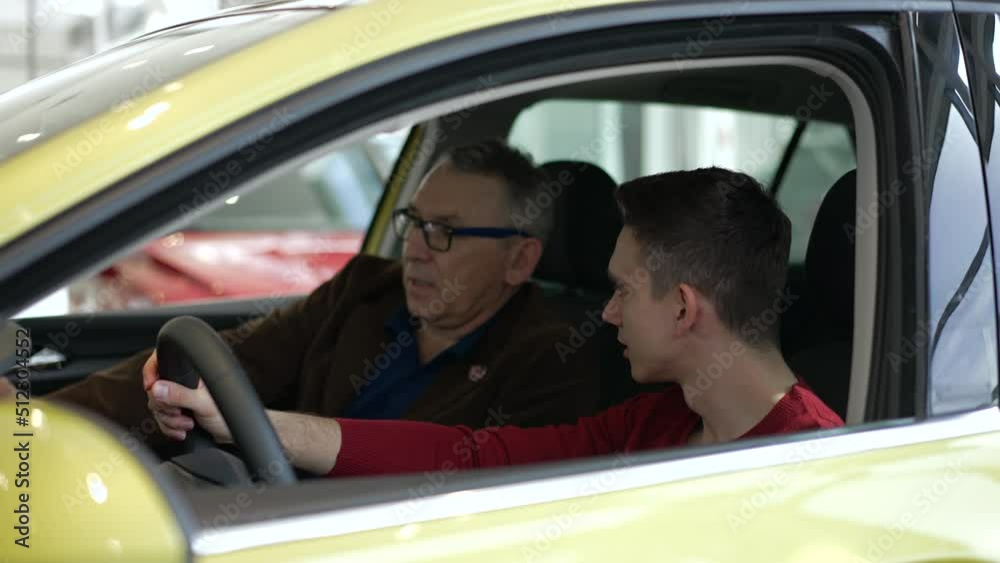 Two male customers are talking and sitting inside new car in modern company spbd. 4k Close view of young son, mature father talk with smiles and examine interior, make decision and sit in transport Two male customers are talking and sitting inside new car in modern company spbd. 4k Close view of young son, mature father talk with smiles and examine interior, make decision and sit in transport