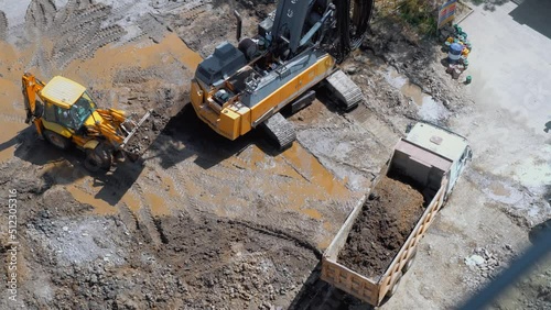 Excavator loads pit onto truck (hydraulic) of heavy construction equipment consisting of boom, bucket and cabin on rotating platform. Construction site of facility. Technique helps person.