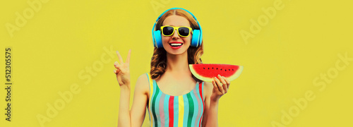 Summer colorful portrait of cheerful happy laughing young woman in headphones listening to music with juicy slice of watermelon on yellow background © rohappy