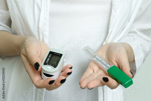 A girl in a white coat holds a thermometer to measure body temperature and a pulse oximeter, covid