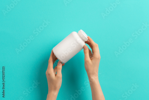 Female hand holding white bottle of medication pills or vitamins or supplements