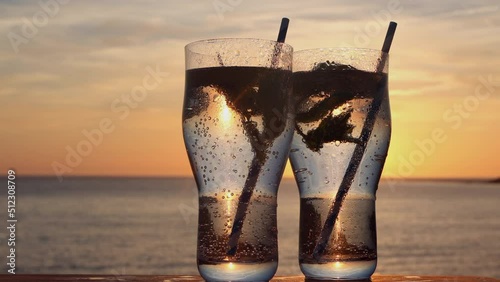 Pair of pint glasses with carbonated water, mint and lemon in Woolacombe Bay at sunset