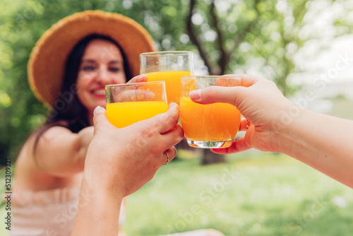 Fototapeta Crop women clinking glasses of juice in park