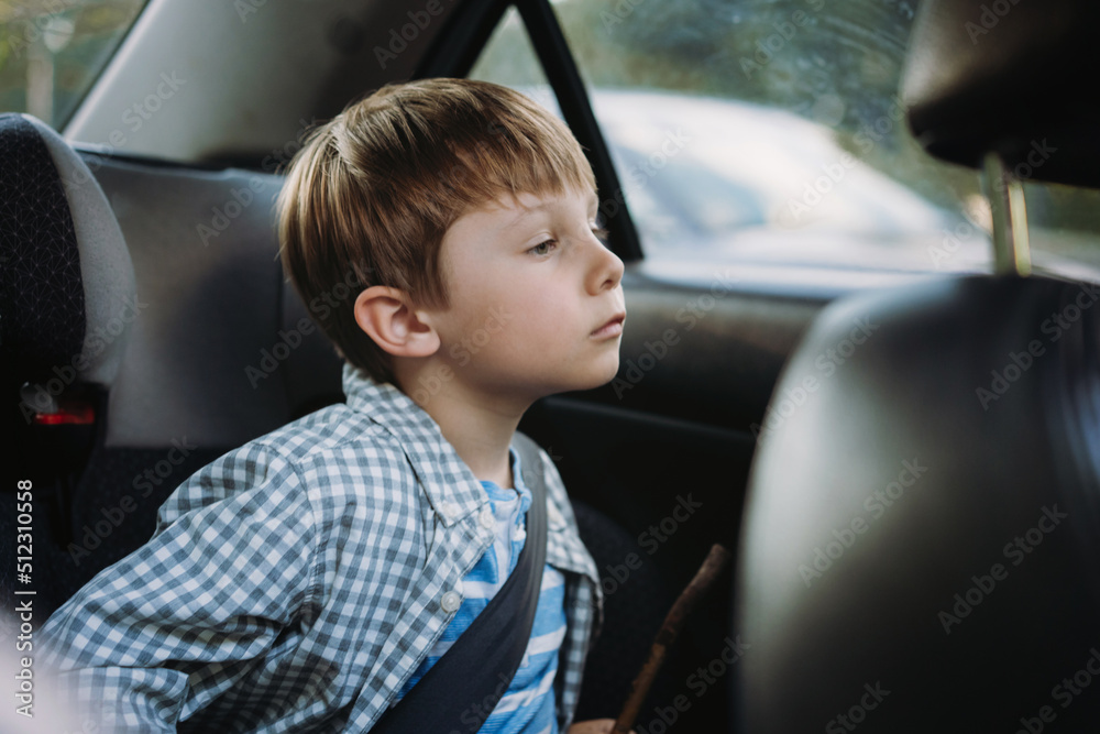 Cute little Caucasian boy sitting in child seat travelling by car tired and bored