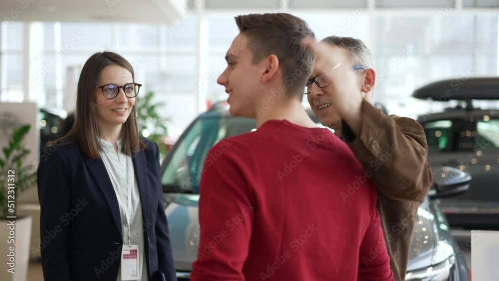Father, son are choosing new car and talking with agent while shopping time in company spbd. 4k Close view of two men talk to female consultant and look with smiles, show joy for camera and stand in Father, son are choosing new car and talking with agent while shopping time in company spbd. 4k Close view of two men talk to female consultant and look with smiles, show joy for camera and stand in