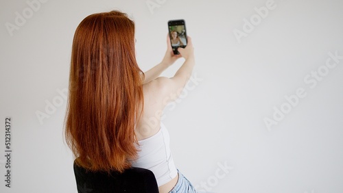 Beautiful young woman takes a selfie photo on the phone. View from the back