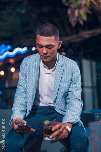 An asian man texting a friend while having a glass of Cuba libre. Lifestyle scene at an al fresco bar. photo