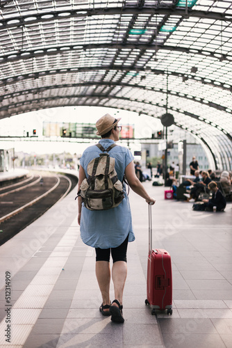 Woman with a hat, suitcase and backpack at the train station