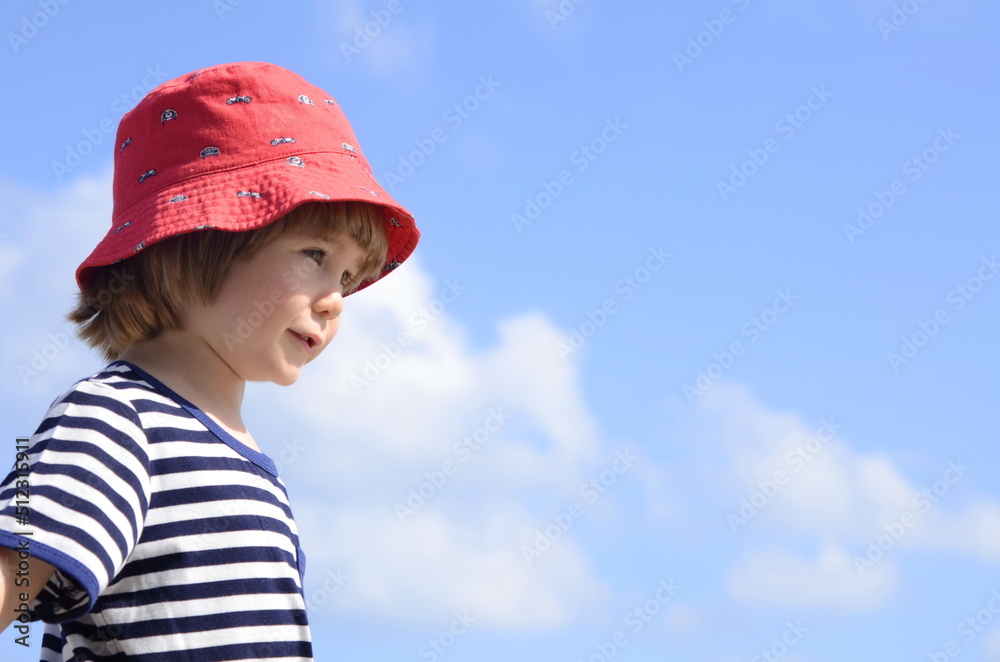 A cute little boy in a vest and a red panama hat against a beautiful sky. Portrait of a child. Travel preparation, family vacation, trip with children. Space for text A cute little boy in a vest and a red panama hat against a beautiful sky. Portrait of a child. Travel preparation, family vacation, trip with children. Space for text