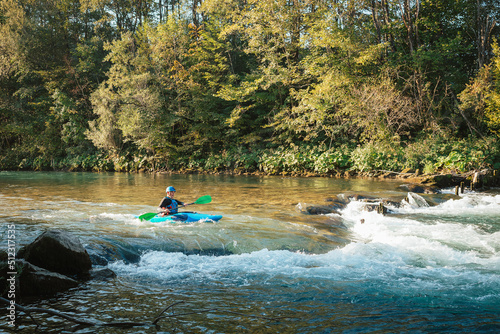 Male recreational athlete paddling carefully over the risky, foamy, and splashy whitewater rapids in his blue kayak