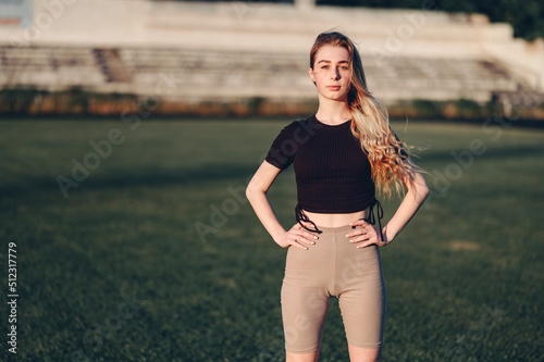 Young Woman Stands Straight Hands on Hips.Girl in Sportswear on Green Grass At the Stadium.