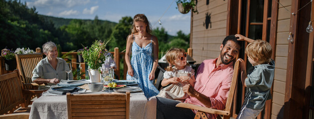Three generation family having fun at barbecue party dinner on patio, people sitting at table on patio with grill.