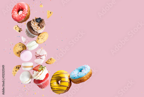 Colorful decorated donuts, chocolate cookies, cupcakes, confectionery and macaroons falling in motion on pink background with sprinkling. Sweet and various pastries flying.