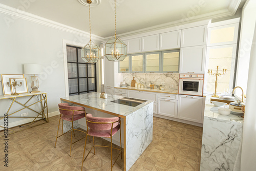 a close view of the white stylish kitchen with a cooking island in the luxurious interior of a modern apartment in light colors with stylish furniture.