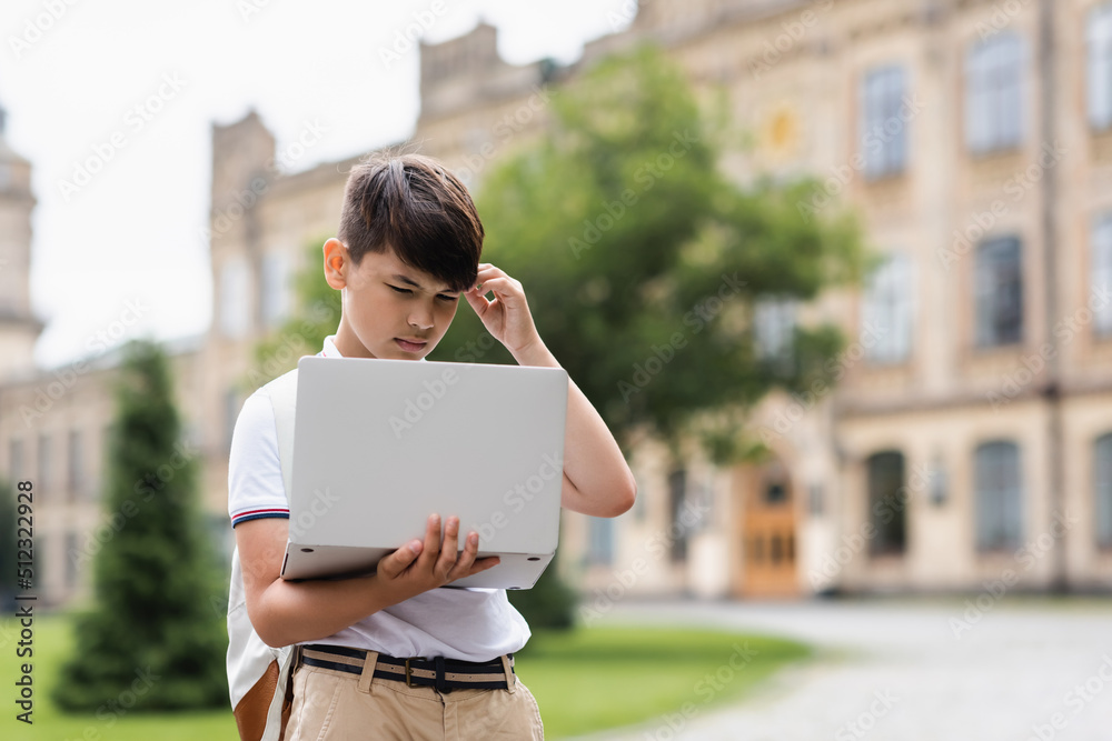 Pensive asian schoolboy looking at laptop outdoors. Pensive asian schoolboy looking at laptop outdoors.