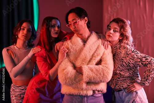 Group of young girls posing with extravagant Asian man in nightclub lit by pink neon light photo