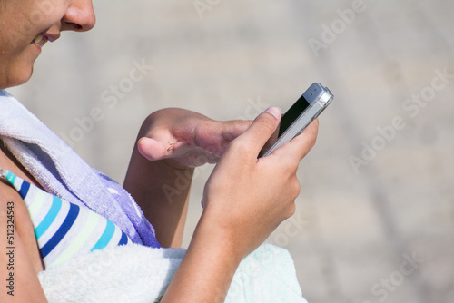 Young teenage girl smiles as she reads the messages on her mobile phone by a swimming pool