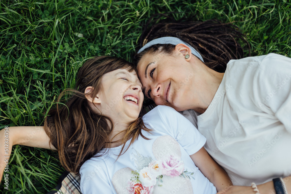 Mother and her daughter lying on the grass and having fun during an outdoor family walk, sunny day Mother and her daughter lying on the grass and having fun during an outdoor family walk, sunny day