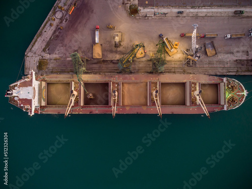 Aerial view of big cargo ship bulk carrier is loaded with grain of wheat in port at sunset