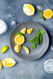lemonade preparationю. glass with ice cubes. fresh ingredients lemon and mint on gray ceramic plate