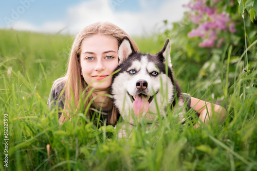 Принти на полотні A Siberian Husky and his beautiful blue-eyed owner are cuddling while lying in the grass