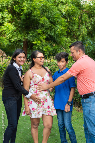 Family touching the belly of a pregnant woman while standing together in the backyard of their home.